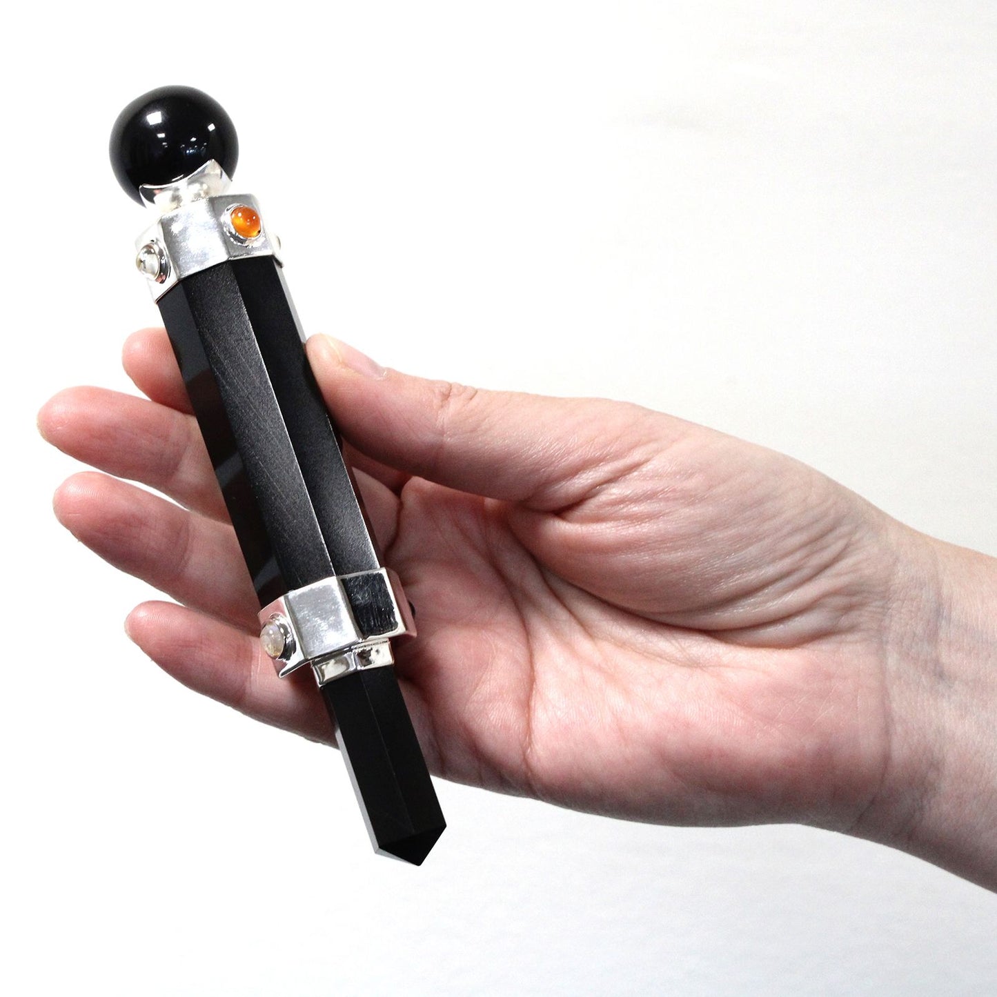 A hand holds a black agate hexagonal crystal healing wand with a black sphere on top.