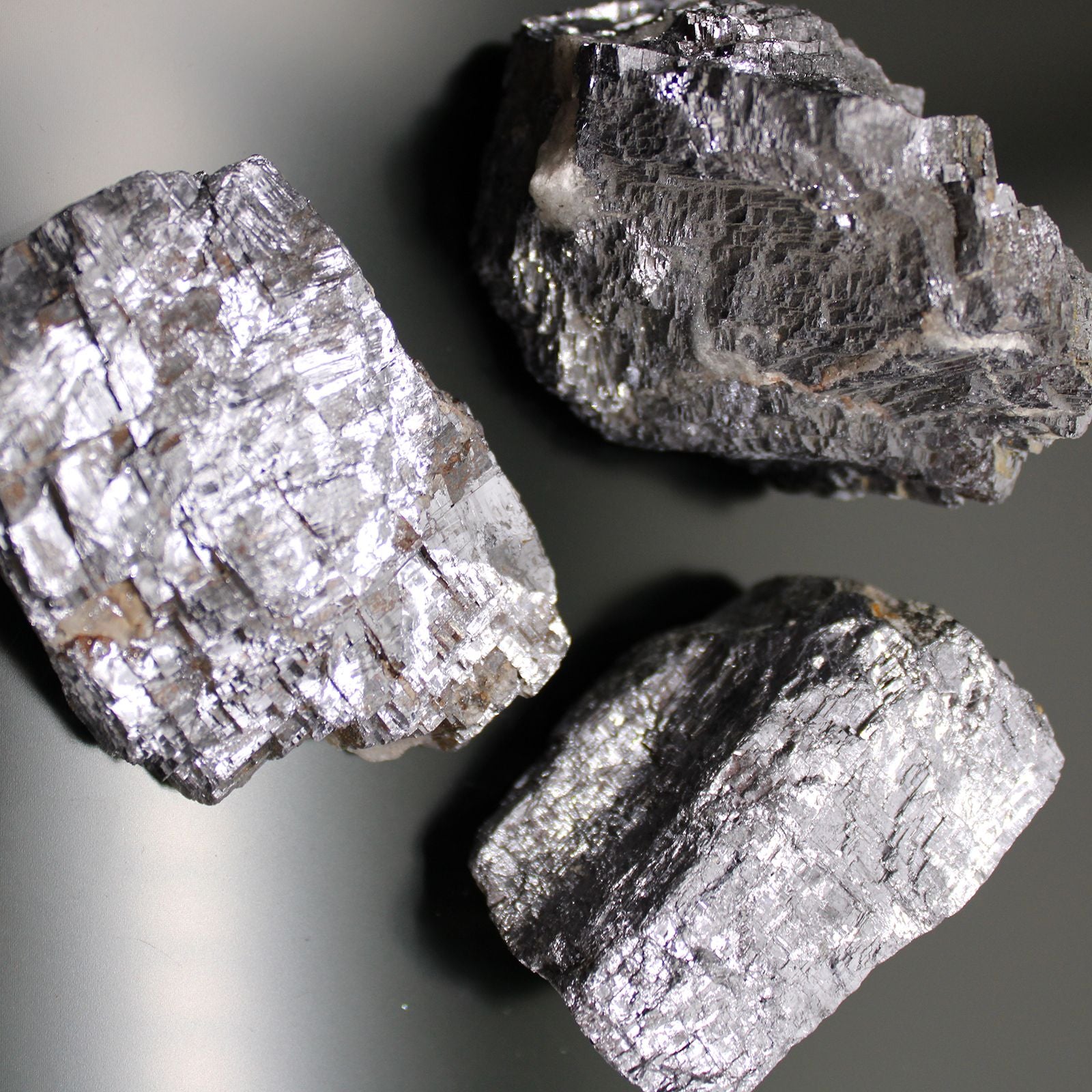 Drei rohe Galena-Mineralien mit metallischem Glanz und kubischer Kristallstruktur.