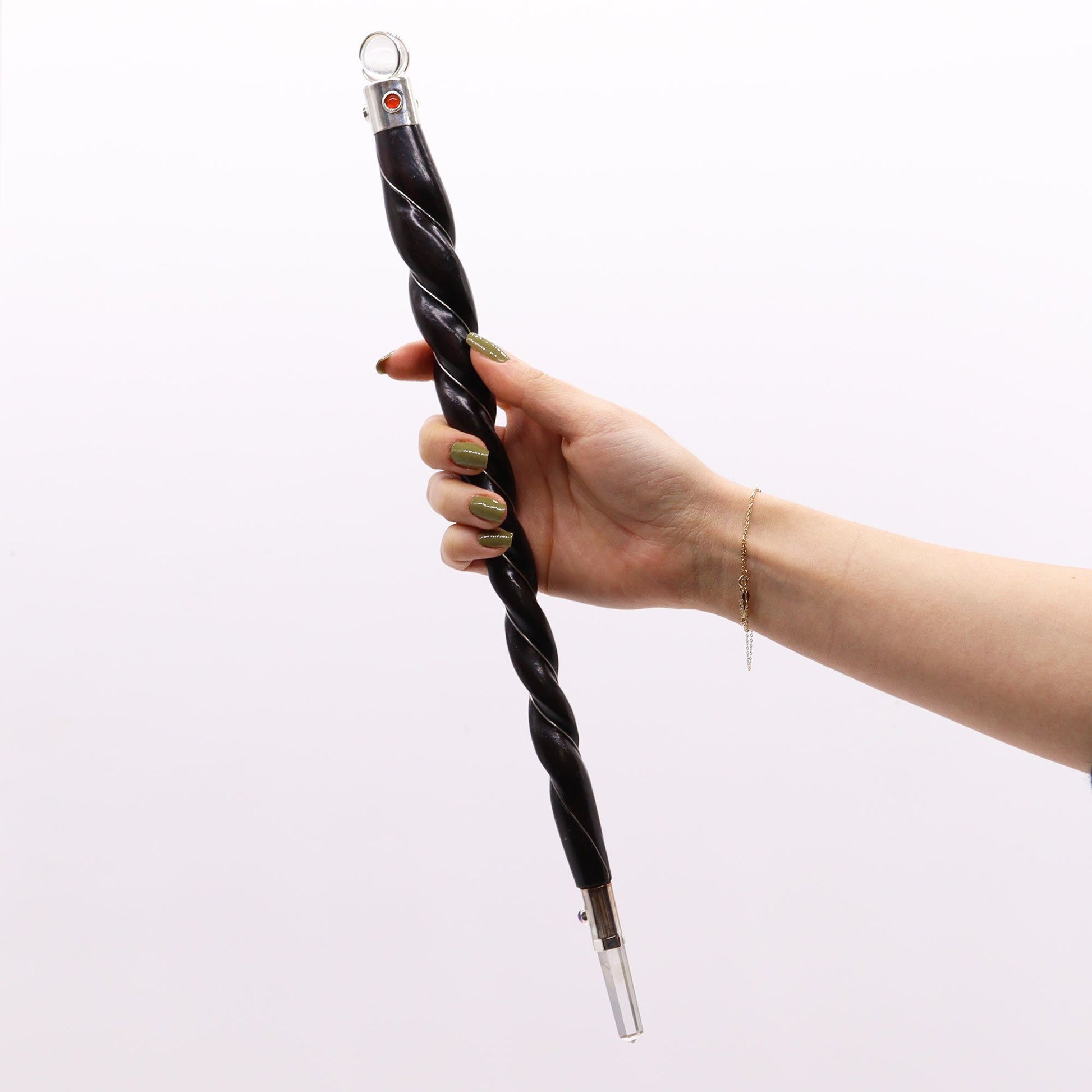 A hand holds a large, twisted dark wood wand with silver wire inlay and a rock quartz tip.