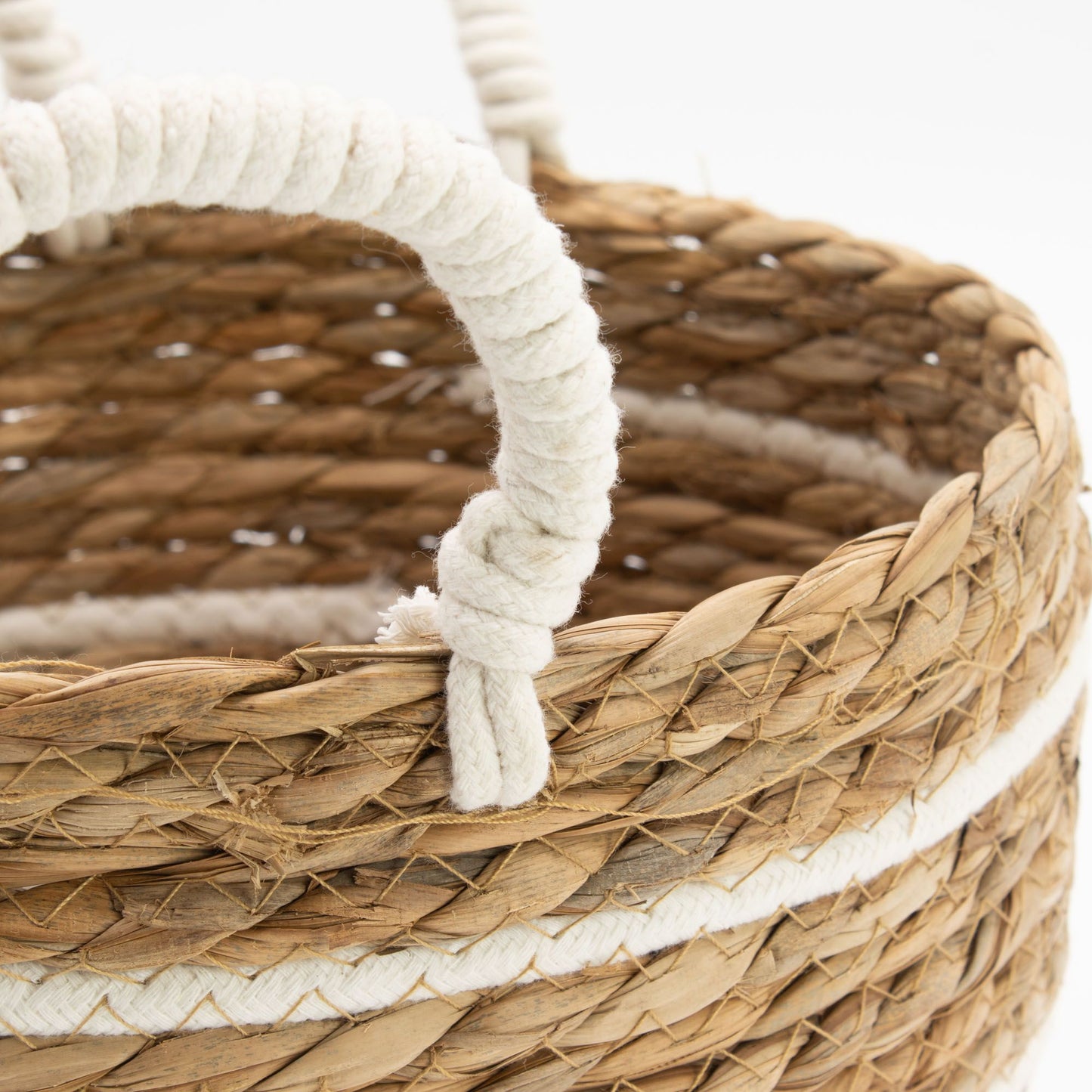 A close-up of a natural seagrass basket with white rope handles and white stripes.