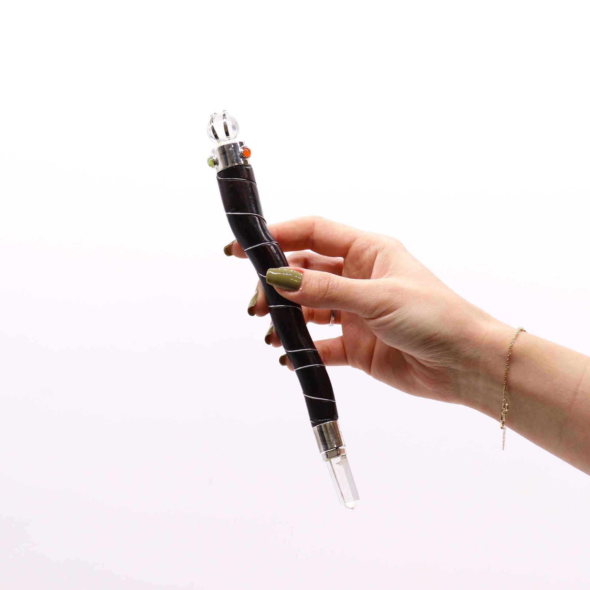 A hand holds a curved dark wood wand with a clear quartz crystal point and decorative beads.