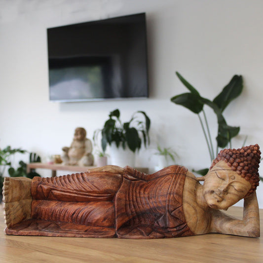 Hand carved wooden sleeping Buddha statue on a wooden surface.