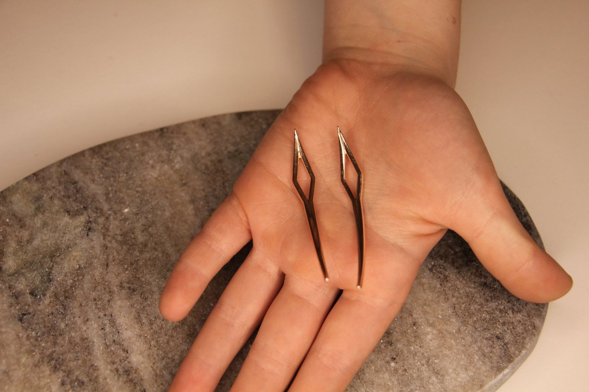 Zwei roségoldene Dreadlock-Nadeln liegen in einer Hand.