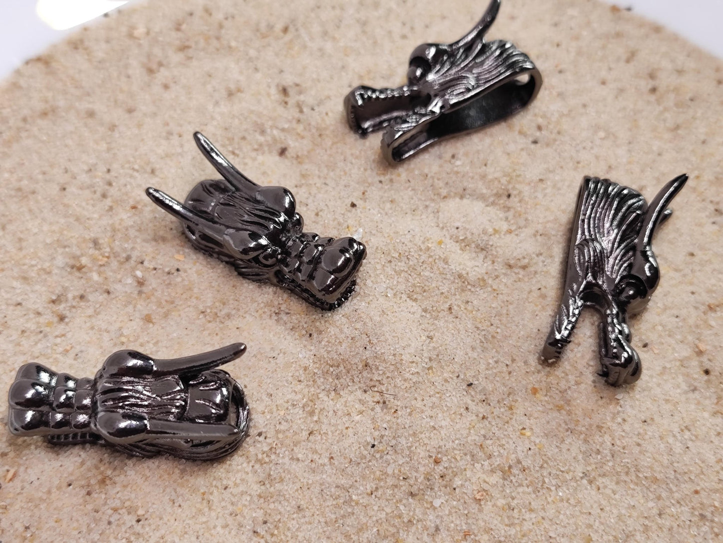 Vier dunkle Drachenkopf-Bartperlen liegen auf Sand.