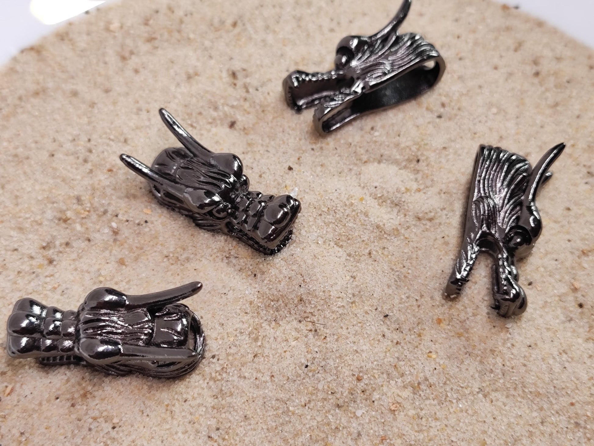 Vier dunkle Drachenkopf-Bartperlen liegen auf Sand.