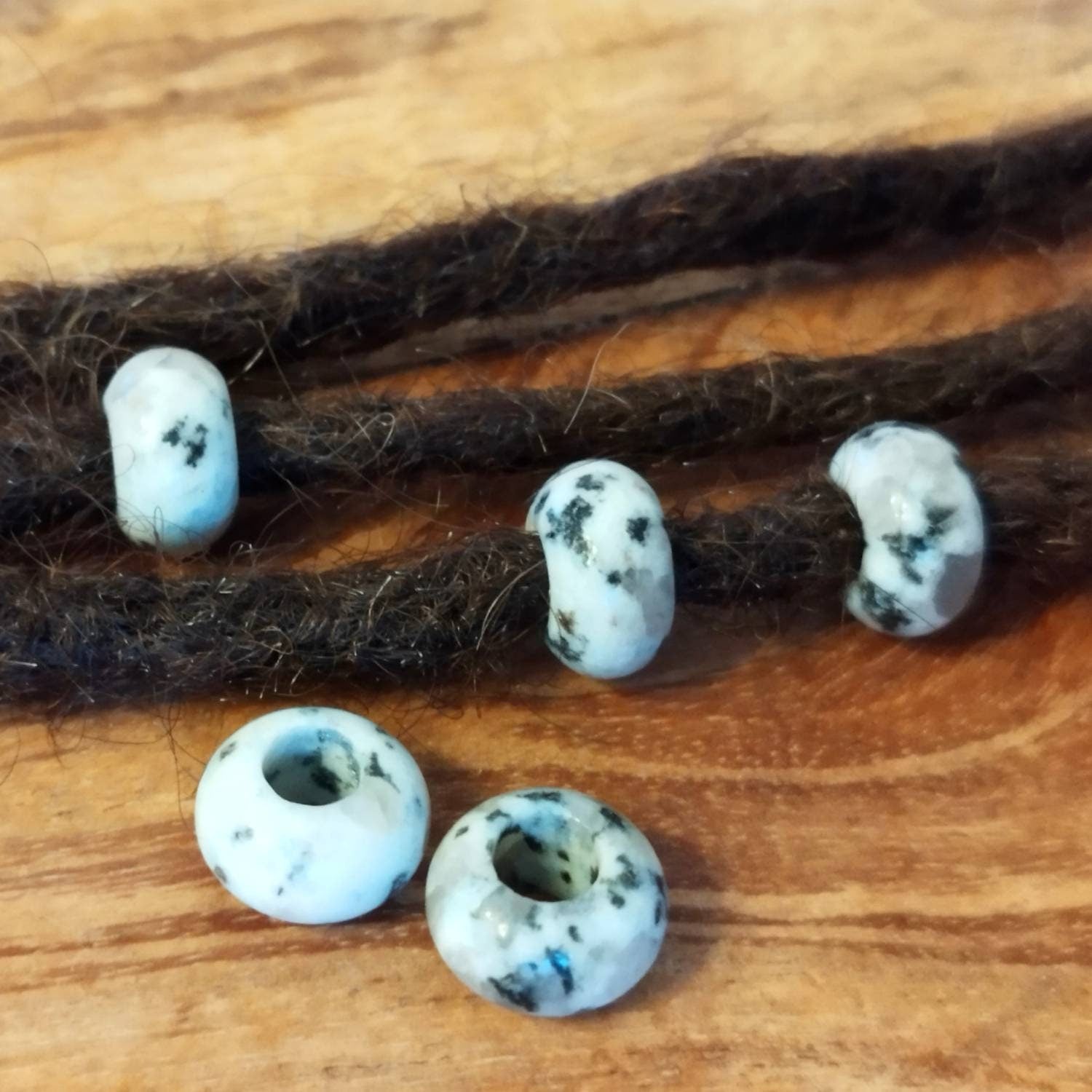 Dreadperlen aus Sesamjaspis Edelstein mit schwarzen Sprenkeln auf Holzuntergrund.