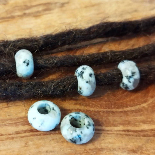 Dreadperlen aus Sesamjaspis Edelstein mit schwarzen Sprenkeln auf Holzuntergrund.