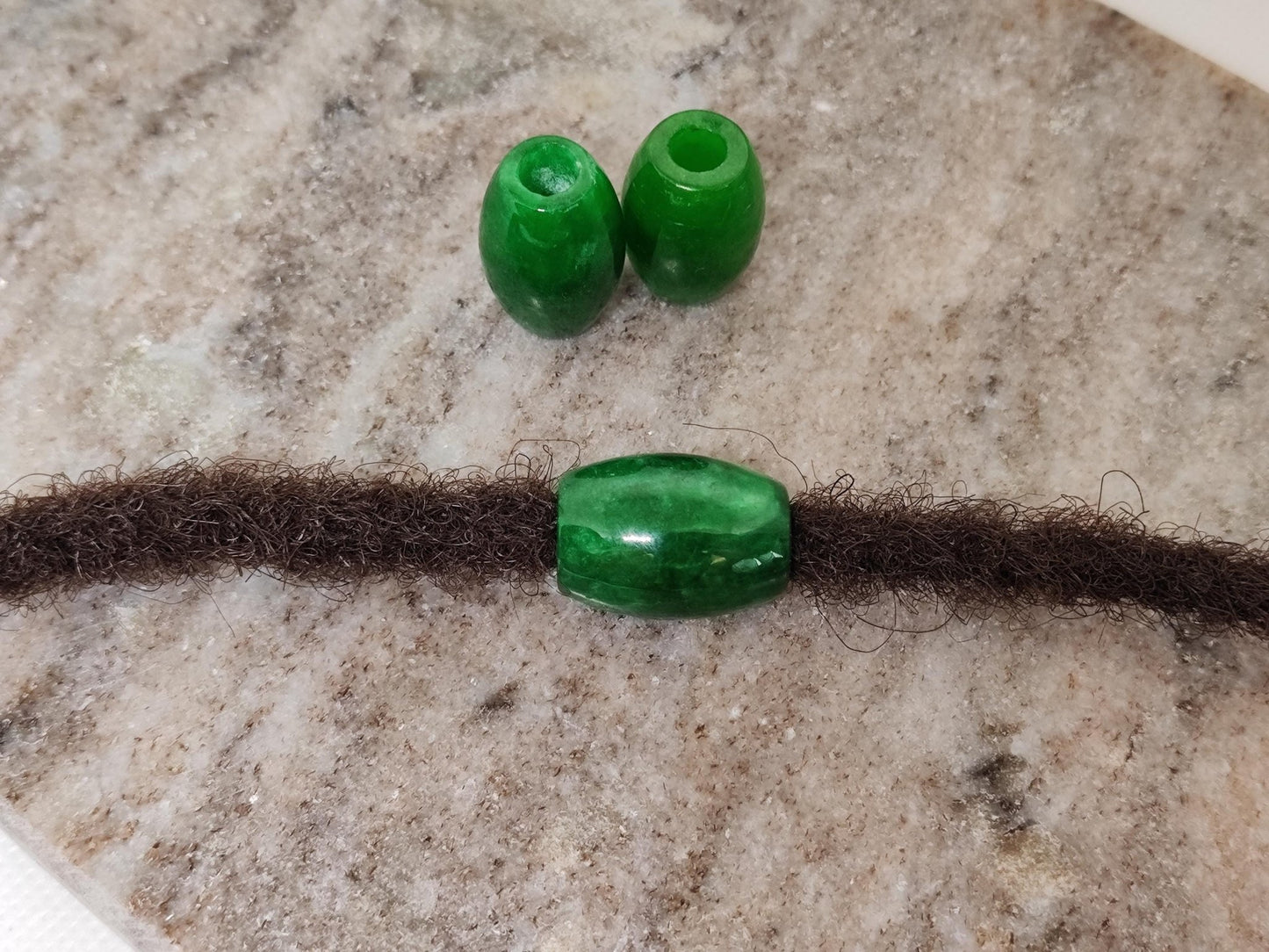 Große Dreadperlen aus burmesischer Jade mit braunem Haarstrang.